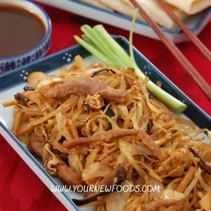 Moo shu pork on a black rectangular dish with spring onion on the side