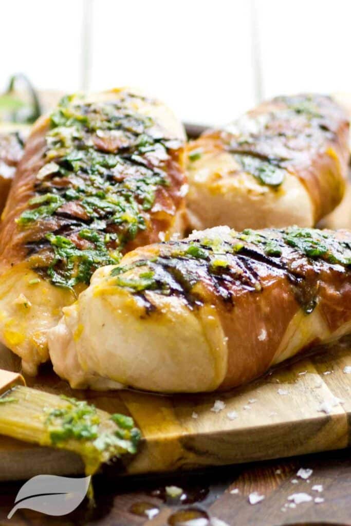 three chicken breasts cooked wth herbs on top on a wooden board