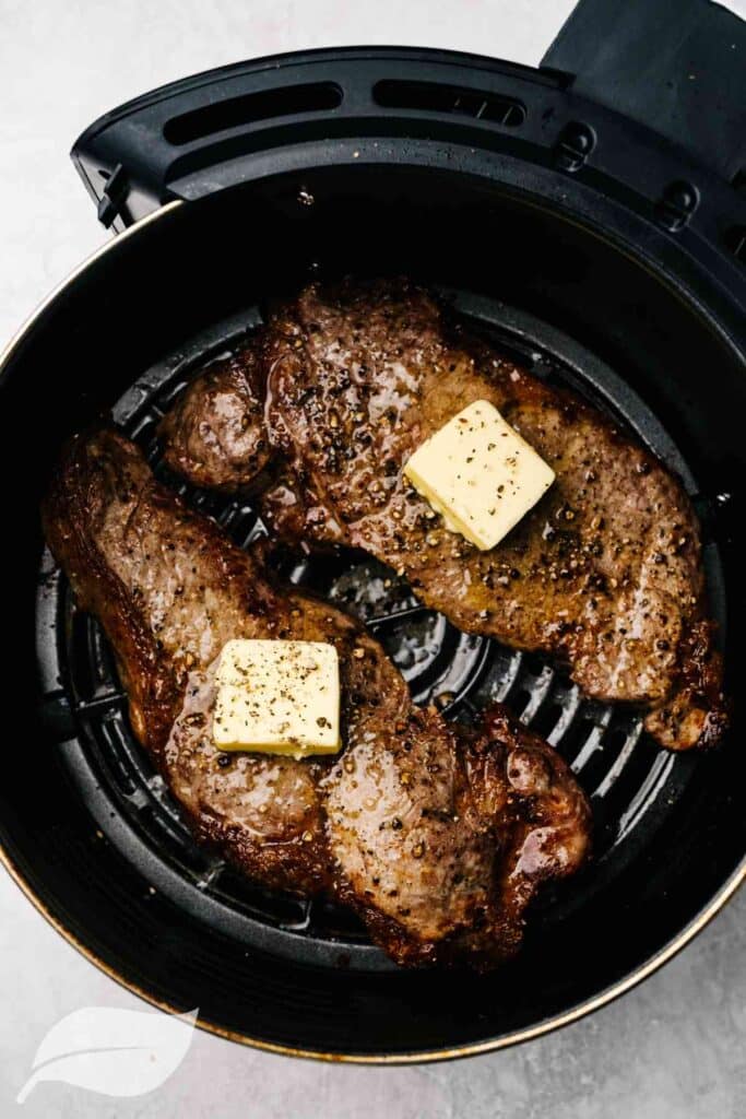 Two Air Fryer Lamb chops in an air fryer basket with a square of butter on them