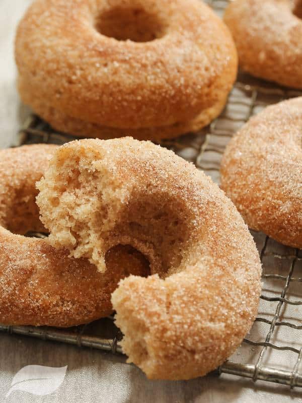 Homemade apple cider donuts on a rack with a bite missing