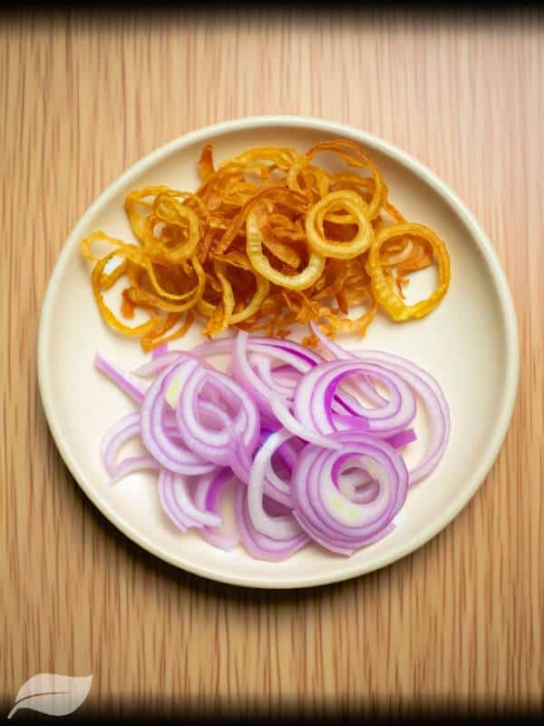 Thinly sliced shallots, both fried and fresh, arranged on a small plate