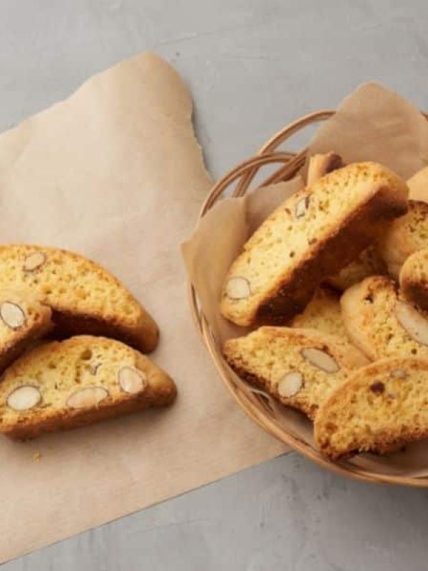 Italian xmas biscotti in a wicker bowl with three pieces on brown paper to the left